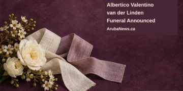 Conceptual memorial illustration of white flowers and blank folded linen ribbons on a plum tabletop, with the article headline and ArubaNews.ca branding; not a photograph of the person or funeral.