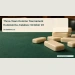 Conceptual editorial illustration of a set of plain ivory domino tiles on a green tabletop with empty chairs softly out of focus, close-up angle, no text, logos or people; not a documentary photograph of the people, venue or event.
