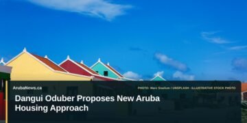 Illustrative stock photo for “Dangui Oduber Proposes New Aruba Housing Approach”: Colorful buildings under a bright blue sky. Photo by Marc Snailum via Unsplash; not a photograph of the specific event. Headline and ArubaNews.ca branding appear in a lower-third news tile.