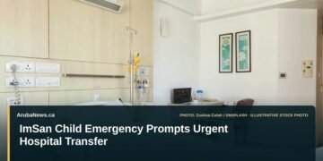 Illustrative stock photo for “ImSan Child Emergency Prompts Urgent Hospital Transfer”: Empty hospital room with bed and desk. Photo by Zoshua Colah via Unsplash; not a photograph of the specific event. Headline and ArubaNews.ca branding appear in a lower-third news tile.