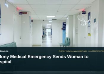 Illustrative stock photo for “Colony Medical Emergency Sends Woman to Hospital”: Empty hospital corridor with benches and doors. Photo by Tasha Kostyuk via Unsplash; not a photograph of the specific event. Headline and ArubaNews.ca branding appear in a lower-third news tile.