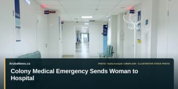 Illustrative stock photo for “Colony Medical Emergency Sends Woman to Hospital”: Empty hospital corridor with benches and doors. Photo by Tasha Kostyuk via Unsplash; not a photograph of the specific event. Headline and ArubaNews.ca branding appear in a lower-third news tile.