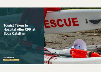 Illustrative stock photograph for “Tourist Taken to Hospital After CPR at Boca Catalina”: 2026-07-10 Vancouver beach lifeguard red jacket carrying surf rescue surfboard. Photograph by Anthony Maw via Unsplash. This is not a photograph of the specific Aruba news event.