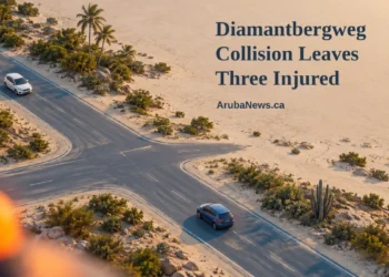 Conceptual editorial illustration, not the actual crash or intersection: two intact cars at a generic Caribbean crossroads, with a blurred amber beacon, the Diamantbergweg headline and ArubaNews.ca branding.