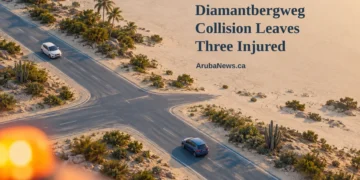 Conceptual editorial illustration, not the actual crash or intersection: two intact cars at a generic Caribbean crossroads, with a blurred amber beacon, the Diamantbergweg headline and ArubaNews.ca branding.