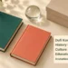 Conceptual editorial still life of two blank hardback books, an archival box and glass paperweight, with the article headline and ArubaNews.ca branding; not the actual donated book covers.