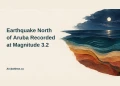Conceptual editorial illustration of moonlit sea bands and layered ochre rock strata with subtle ripple lines, the earthquake headline, and ArubaNews.ca branding; not an epicentre map or incident photograph.