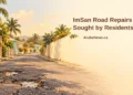 Conceptual editorial illustration of a worn Caribbean neighbourhood road with potholes, not the actual ImSan road, with a residents’ repair-appeal headline and ArubaNews.ca branding.