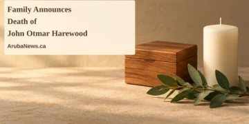 Family Announces Death of John Otmar Harewood Conceptual memorial illustration of an unmarked wooden keepsake box, an unlit candle and green leaves on a sandy tabletop, with the article headline and ArubaNews.ca branding; no portrait or documentary scene.