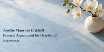Conceptual memorial illustration of white orchids in a plain ceramic vase on a pale blue tabletop, with the article headline and ArubaNews.ca branding; not a photograph of the person or funeral.