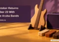Conceptual editorial illustration of a wooden guitar form, plain amplifier and rhythm blocks on an ochre tabletop, with the article headline and ArubaNews.ca branding.
