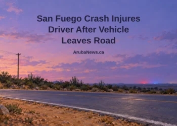 Painterly conceptual editorial illustration, not the actual crash or location: empty Caribbean road beside cactus hedges and an upright utility pole under a lavender sky, with the San Fuego headline and ArubaNews.ca branding.