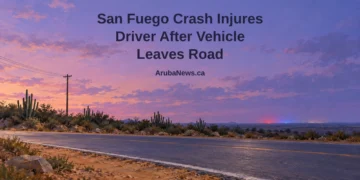 San Fuego Crash Injures Driver After Vehicle Leaves Road Painterly conceptual editorial illustration, not the actual crash or location: empty Caribbean road beside cactus hedges and an upright utility pole under a lavender sky, with the San Fuego headline and ArubaNews.ca branding.