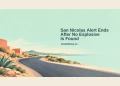 Conceptual editorial illustration of an empty curving road, stylized terracotta shapes and aloe beside a pale mint sky, with the resolved-alert headline and ArubaNews.ca branding; not the actual San Nicolas location or incident.
